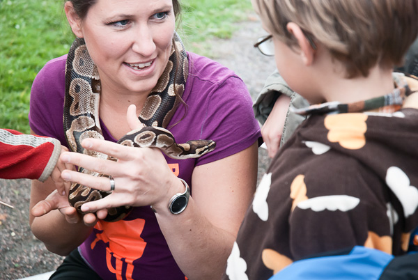 En person sitter med en orm runt halsen och pratar med ett barn som står bredvid.