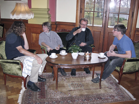 Fyra personer sitter runt ett bord och pratar och dricker kaffe.