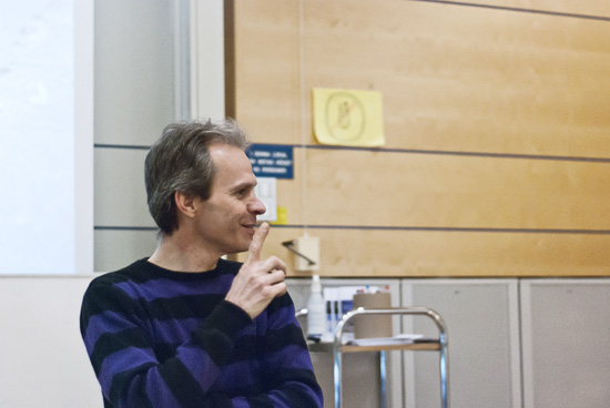 En person står längst fram i en föreläsningssal och håller ett finger framför munnen.
