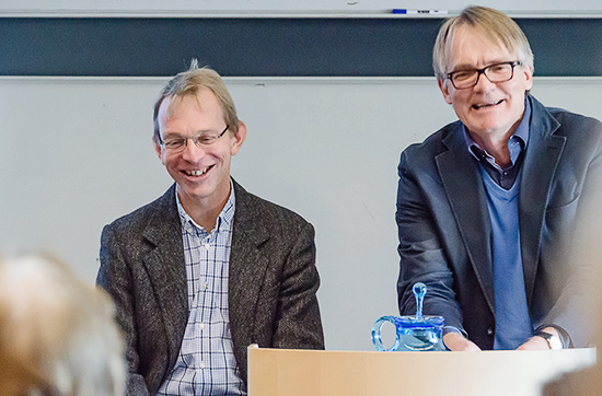 Två leende personer sitter bredvid varandra längst fram i en föreläsningssal.