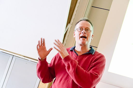 En person står och gestikulerar längst fram i en föreläsningssal.