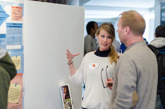 Two people are standing talking in front of a poster.