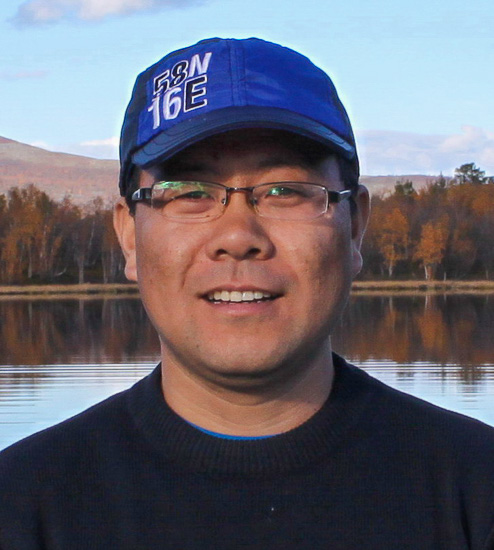 Portrait of a person outside with a lake and a mountain in the background.