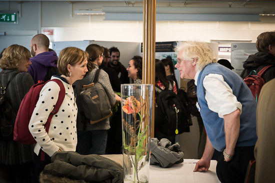 Two people are talking over a table with a lot of people in the background.