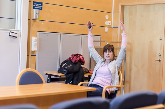 En person sitter längst fram i en föreläsningssal och sträcker upp sina händer.