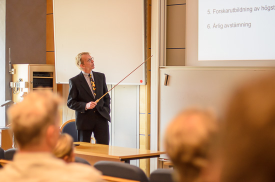 En person står längst fram i en föreläsningssal och pekar med en pekpinne.