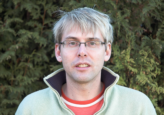 A portrait of a person standing outside against a green background.