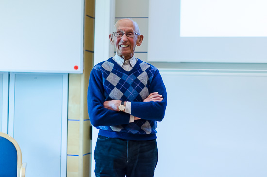 En leende person står med korslagda armar längst fram i en föreläsningssal.