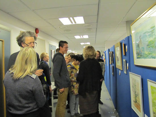 A lot of people are standing in a corridor looking at paintings.