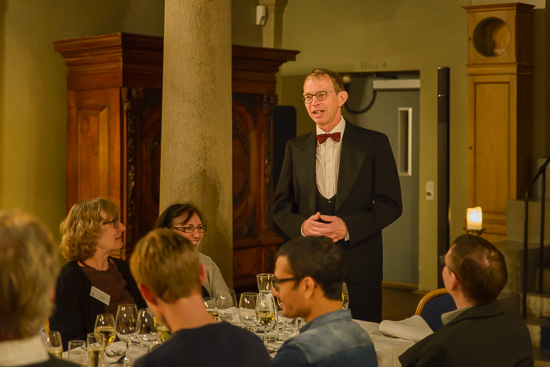 A person is standing up talking beside a dinner table.