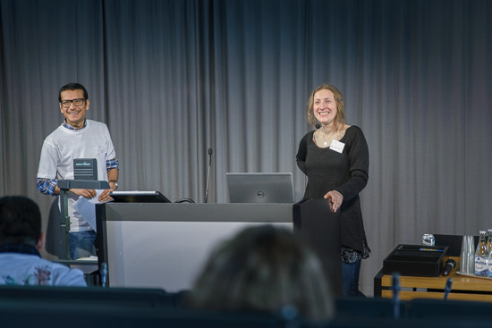 Two people are standing in the front of a lecture hall.