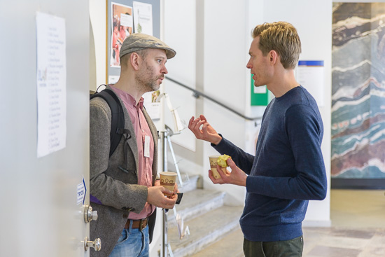 Two people are standing and discussing during a coffee break.