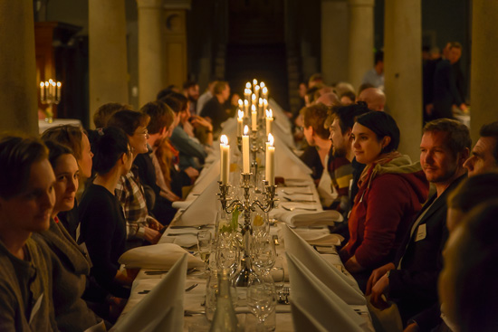 A lot of people are sitting around a dinner table with candles.