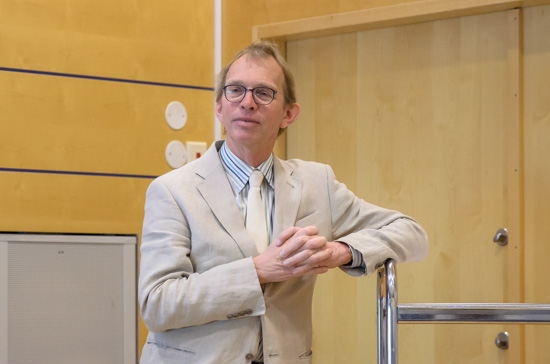 A person is standing leaning on a stand in a lecture hall.