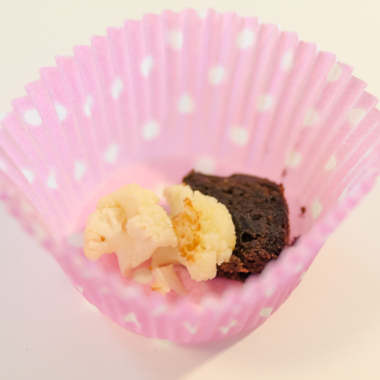 En liten bit blomkål tillsammans med en liten bit brownie i en muffinsform.