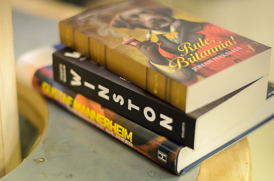 Tre böcker ligger i en hög. Underst ligger en bok där det står något suddigt och sedan texten Mannerheim. Mellan boken står det Winston på ryggen och på den översta boken står det Rule Britannia! på framsidan.