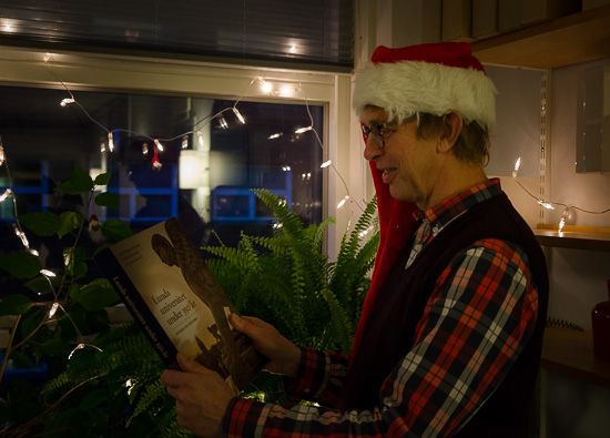 A person in a Christmas hat is standing holding a book in front of Christmas lighting.