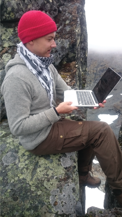 A person is sitting with a laptop on a cliff