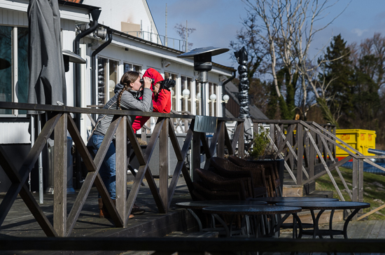 Two people are standing with binoculars on a terrace. 