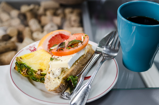 A cup of coffee and plate with a sandwich and fruit.