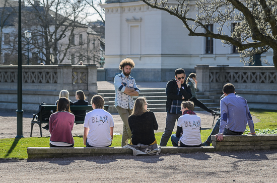 Some persons are standing and sitting outside. Photo.