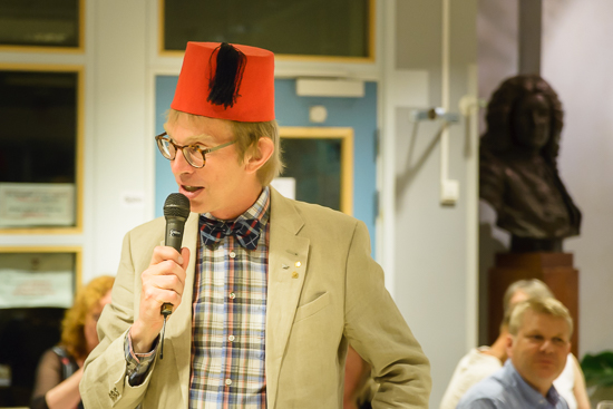 En person står upp med en fez på huvudet och en mikrofon i handen.