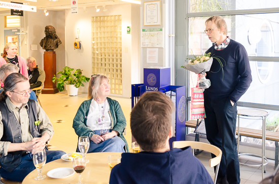 Some people sitting. A man is standing holding flowers.