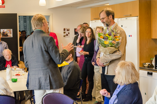 A man stands holding flowers with persons standing around.