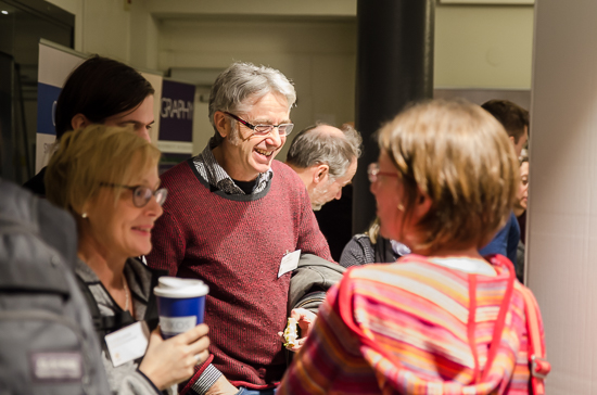 Some smiling persons stand talking and drinking coffee.