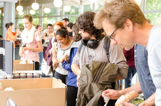 Many persons stand in a line waiting for food.