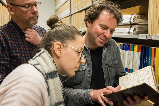 Three persons stand looking in a book.