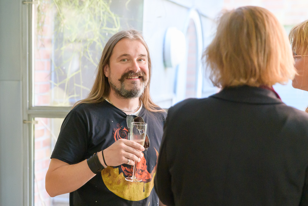 Person with long hair, mustasche and beard smiles into the camera knowing he'll soon be at Copenhell. Photo.