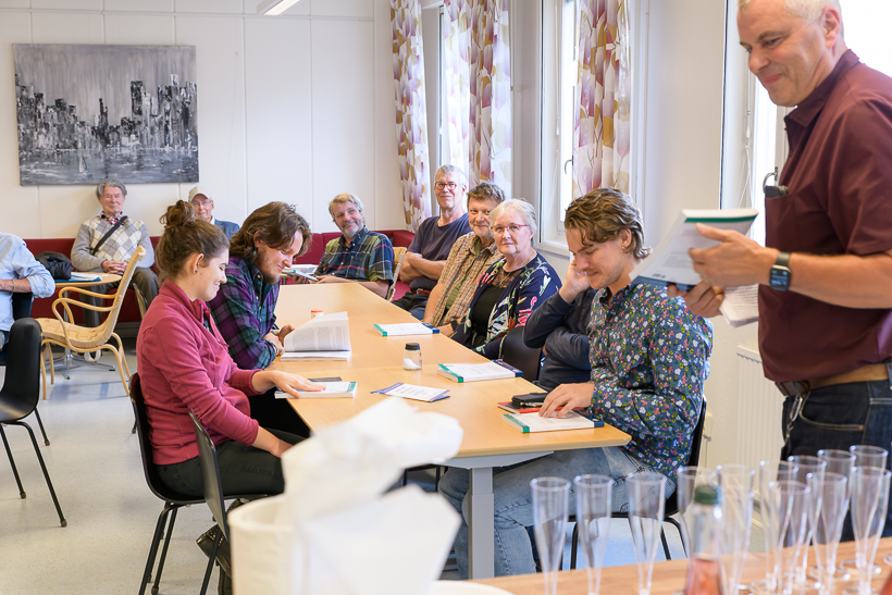 Flera personer sitter vid ett bord och tittar i böcker. Foto.