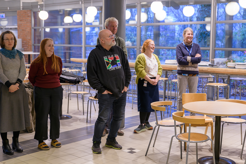 Flera skrattande personer, en av dem håller tal. Foto.