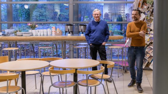 Två personer står framför ett bord med kaffe och tårta. Foto.